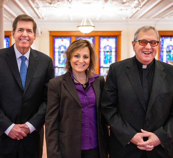 مجموعة من خمسة أشخاص يقفون معًا في ممر مستشفى مضاء بإضاءة ساطعة، ويبتسمون للكاميرا. اثنان يرتديان سماعات طبية وملابس طبية، وواحد يرتدي قميصًا رياضيًا من جامعة غونزاغا، والآخرون يرتدون ملابس غير رسمية أو مهنية، مما يمثل مزيجًا من الطلاب والمهنيين الصحيين.